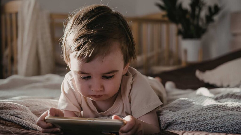 A child on a bed staring at a screen, showing that a reason why a toddler doesn’t respond to their name is that they are deeply distracted.