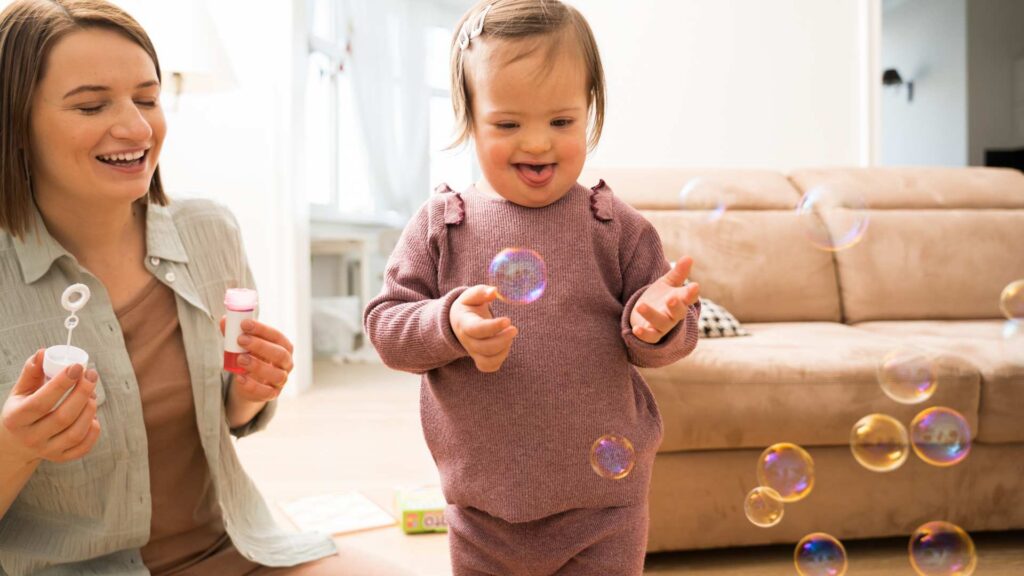 A toddler and adult playing with bubbles, showing a joyful moment to help illustrate learning about the signs of autism at 18 months