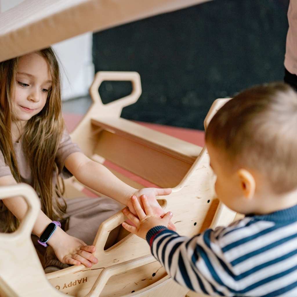 A toddler and an older child play together. This scene shows the child looking toward someone calling them, highlighting early communication development