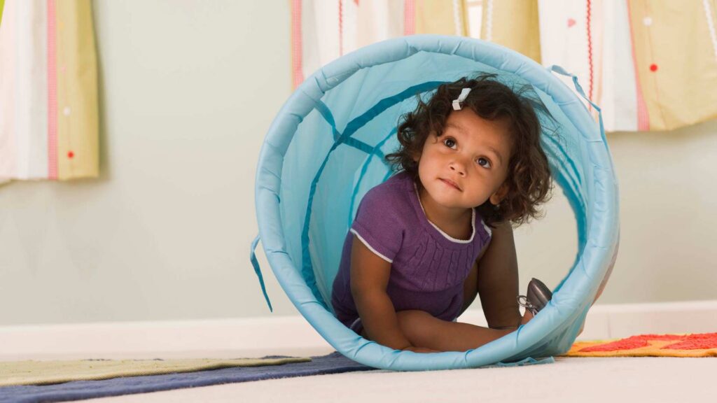 A toddler crawling through a tunnel, showing toddler developmental milestones like movement, curiosity, and play, and representing the question Is My 18-Month-Old Behind