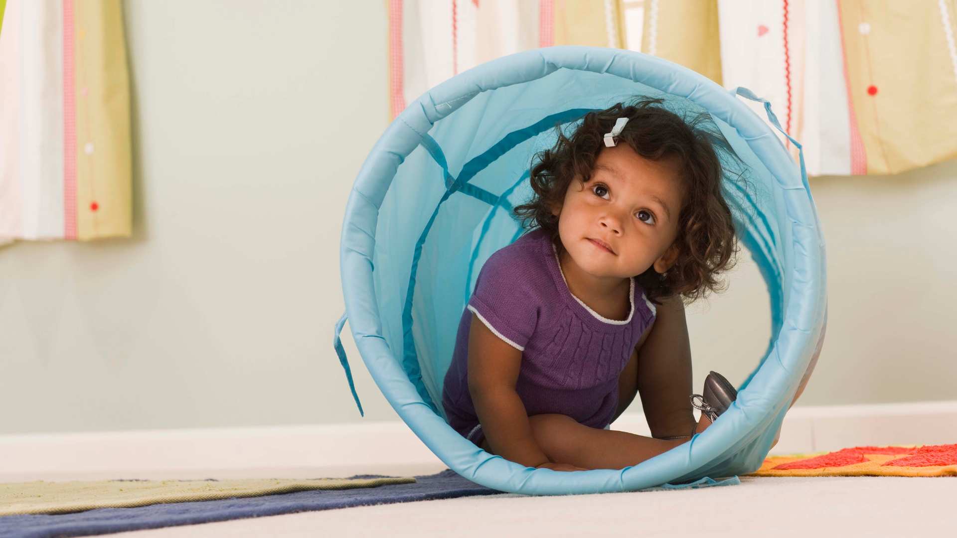 A toddler crawling through a tunnel, showing toddler developmental milestones like movement, curiosity, and play, and representing the question Is My 18-Month-Old Behind