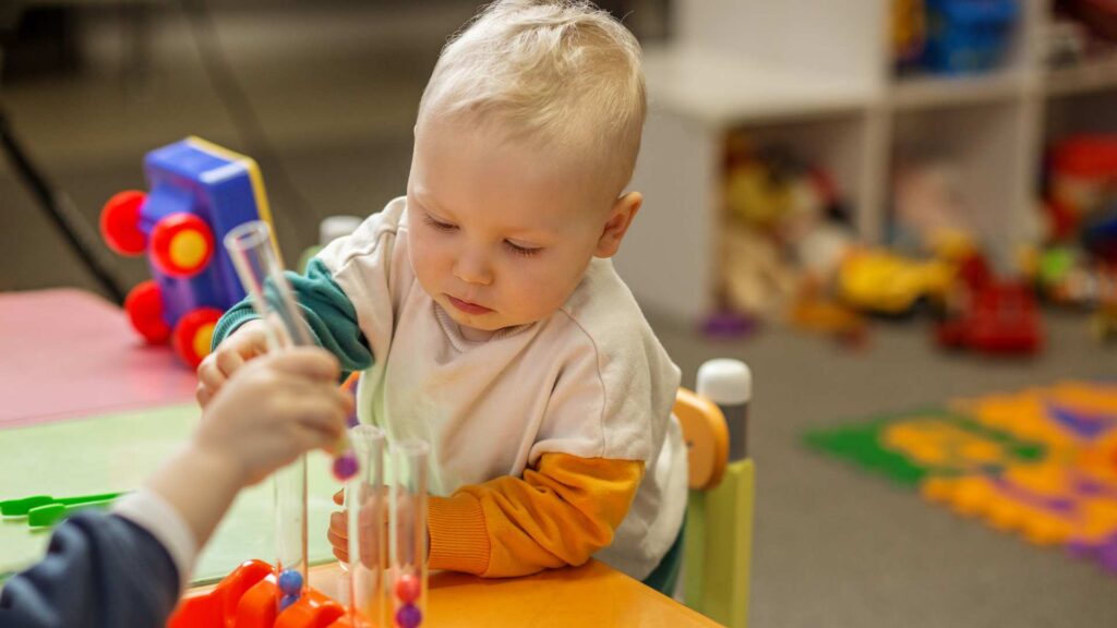 A toddler focused on toys in a playroom. Illustrating Signs of Autism at 12 Months, such as less interest in people