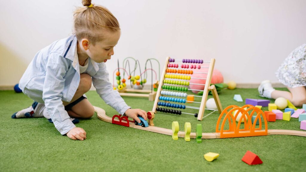 A toddler plays with a wooden train and simple toys, showing the steady, repeated actions in repetitive play, common in early childhood