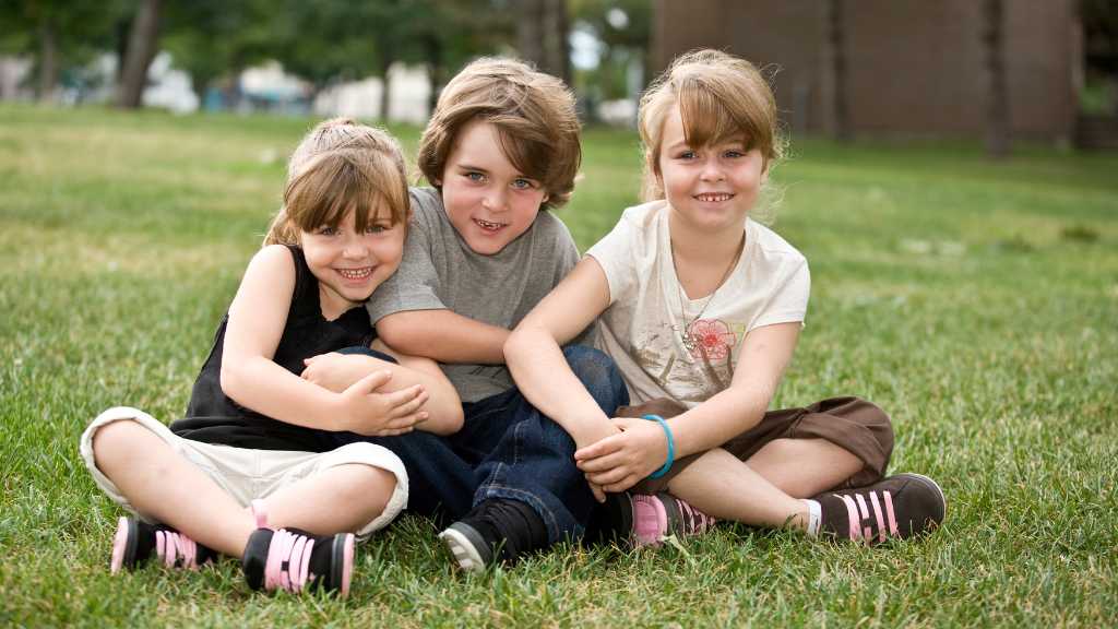 Three siblings sitting together on the grass — autism siblings facing challenges and supporting each other.