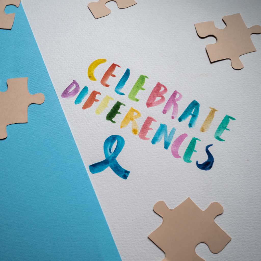 Bright text reading “Celebrate Differences” surrounded by tan puzzle pieces and a blue awareness ribbon
