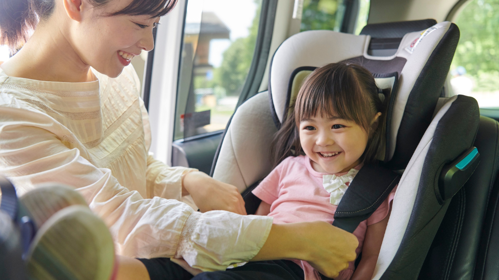 Parent buckling a smiling child into a car seat, illustrating car seat sensory issues in autism and supportive travel strategies.