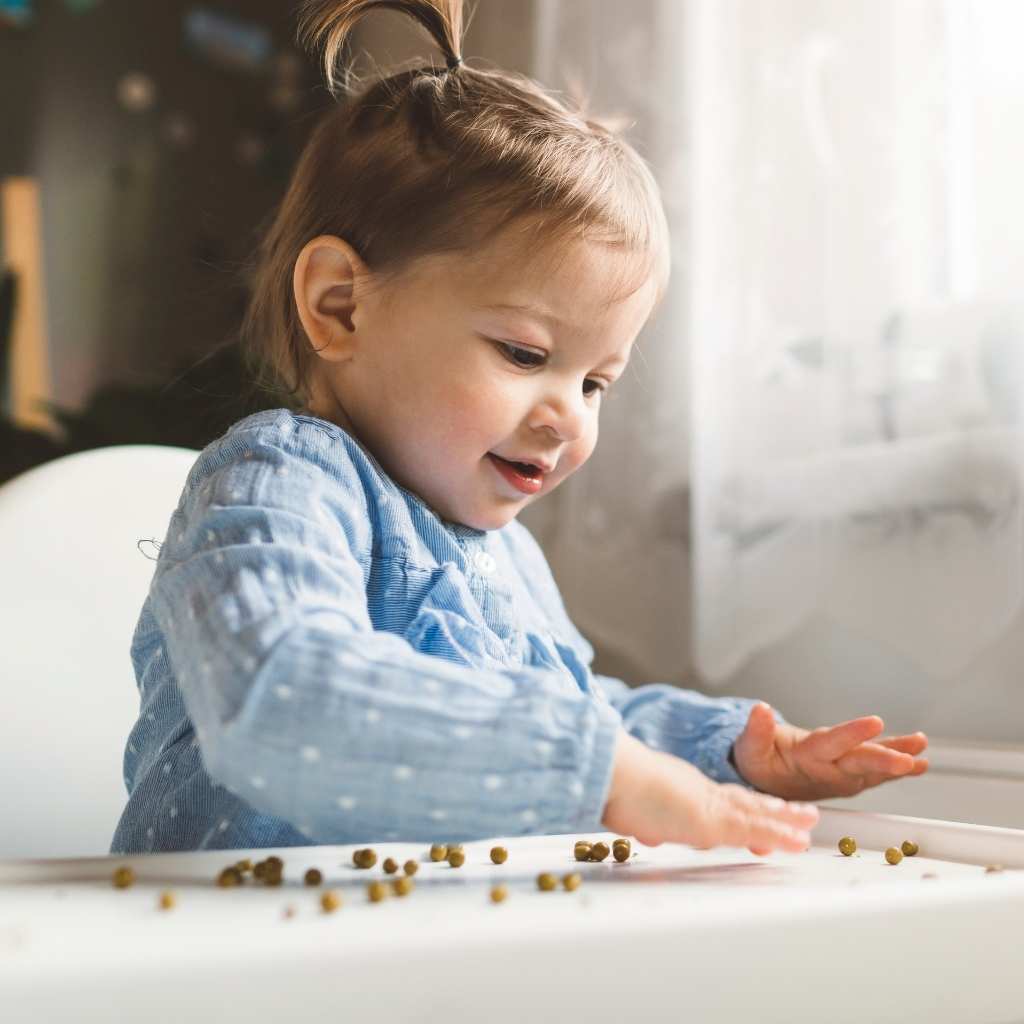 Child exploring tiny pieces of food with their hands. This image supports the topic 'Is My 18-Month-Old Behind' by showing early toddler developmental milestones like grasping and curiosity