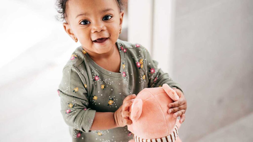 Autism support groups: a toddler in green pajamas smiling and holding a teddy bear.