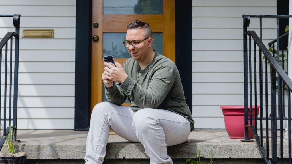 An adult man sits on his doorsteps and reviews his RAADS-R test results on his phone