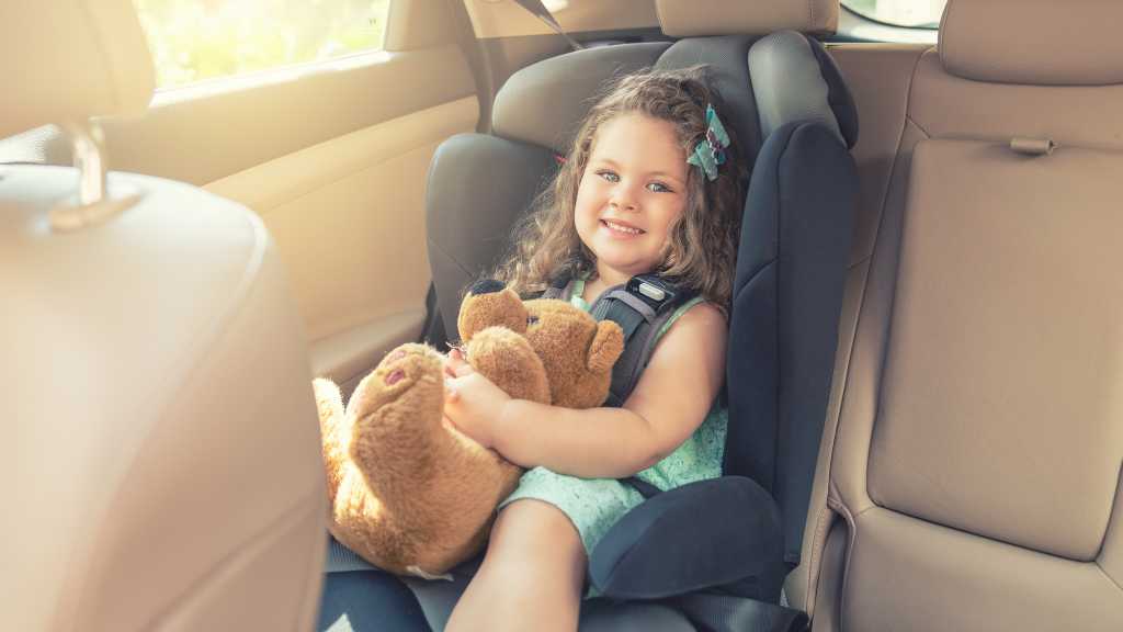 Car Seat Sensory Issues in Autism: A Supportive Guide for Parents and Caregivers 2 Smiling child sitting calmly in a car seat holding a teddy bear, illustrating ABA therapy support for car seat sensory issues in autism.