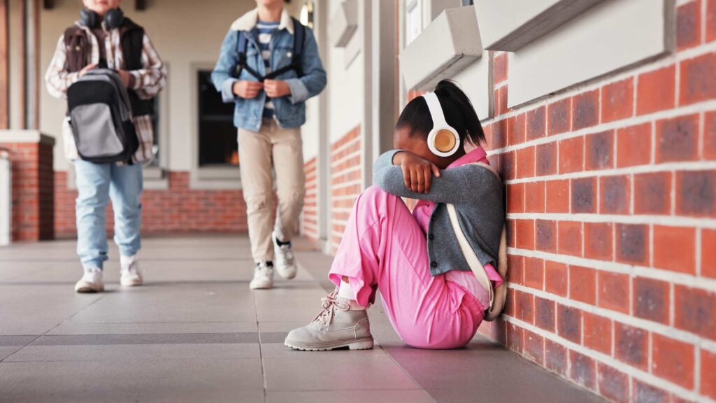 Student sitting on the ground with knees pulled close and headphones on, capturing a moment of overwhelm related to autism and mental health
