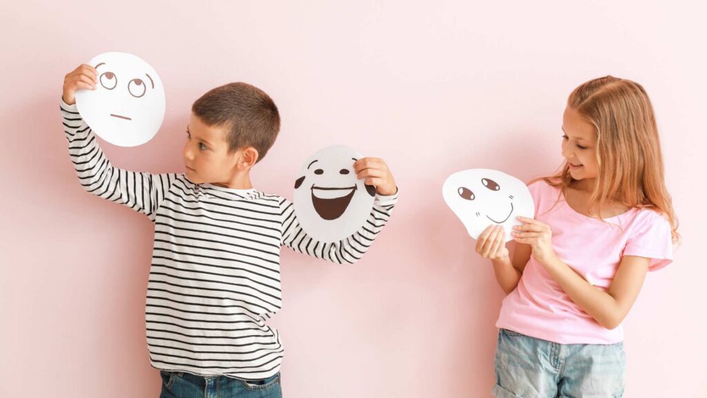 Two children holding simple face cutouts, showing how autistic traits can appear in different ways for girls and boys