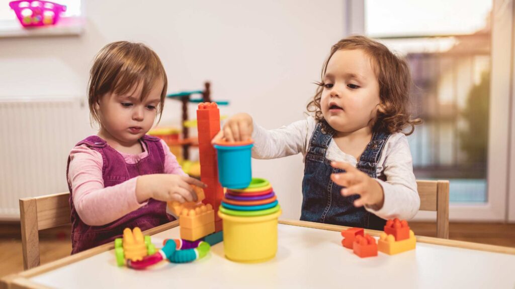 Two toddlers stacking toys and blocks, shown as a visual backdrop for information on signs of autism at 18 months