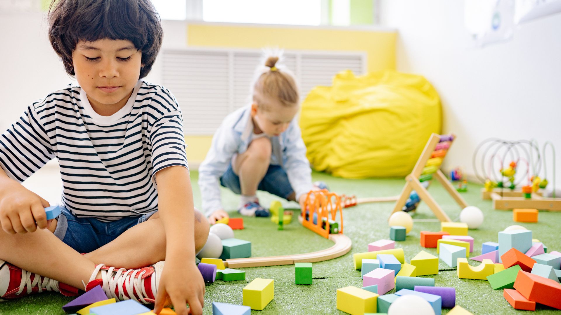 Blog 8 Two young children play separately with toys in the same room, illustrating signs of autism at age 3, such as not showing interest in peers.