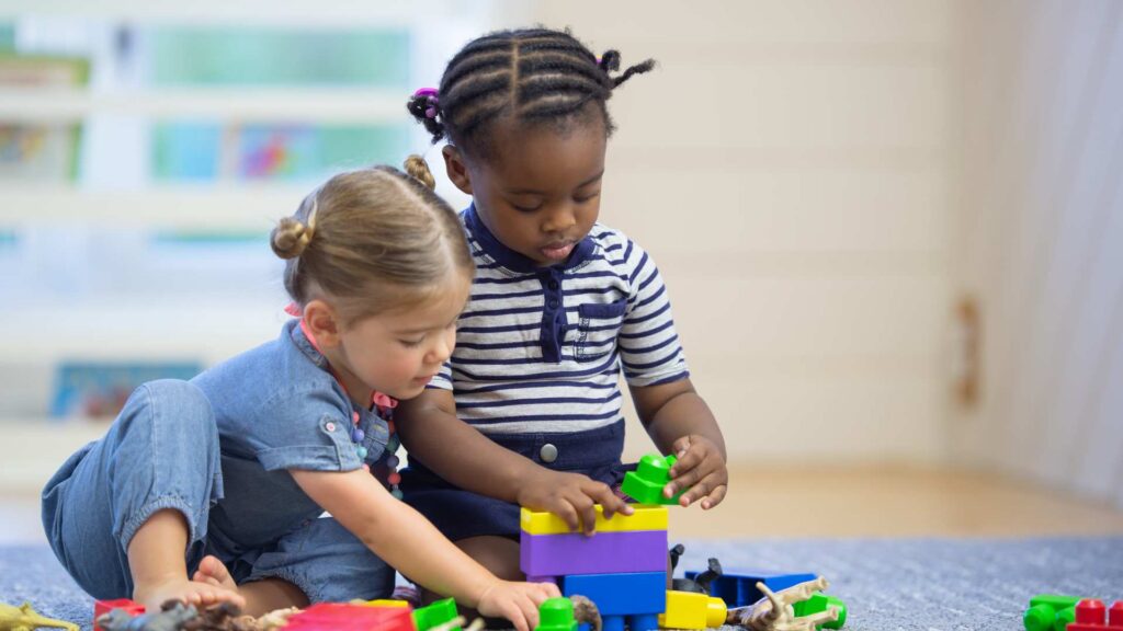 Two young children playing with bright blocks. This visual helps explore the question Is My 18-Month-Old Behind by showing common toddler developmental milestones