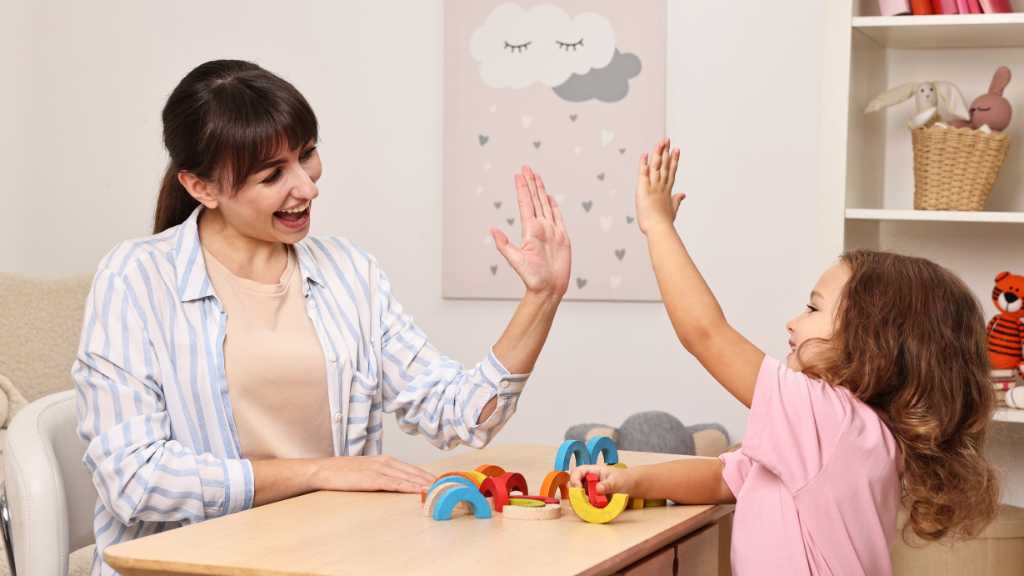 Therapist giving a high five to a young child during a learning session, symbolizing support and understanding across different levels of autism.