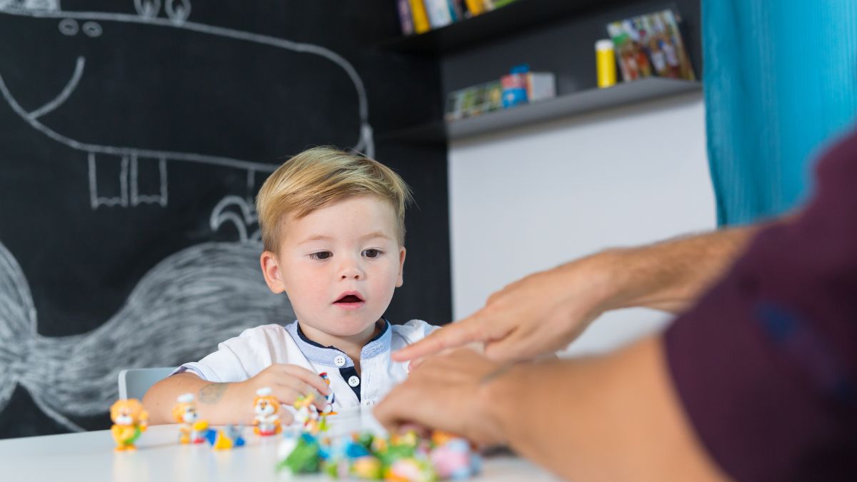 Blog 4 A toddler is mesmerized as a therapist arranges his toys