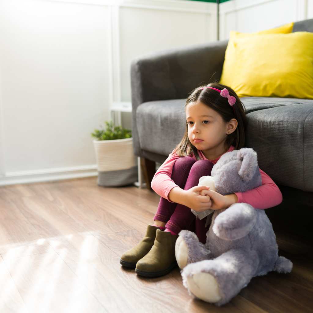 Young child hugging a plush toy while sitting alone, suggesting autism and emotional support