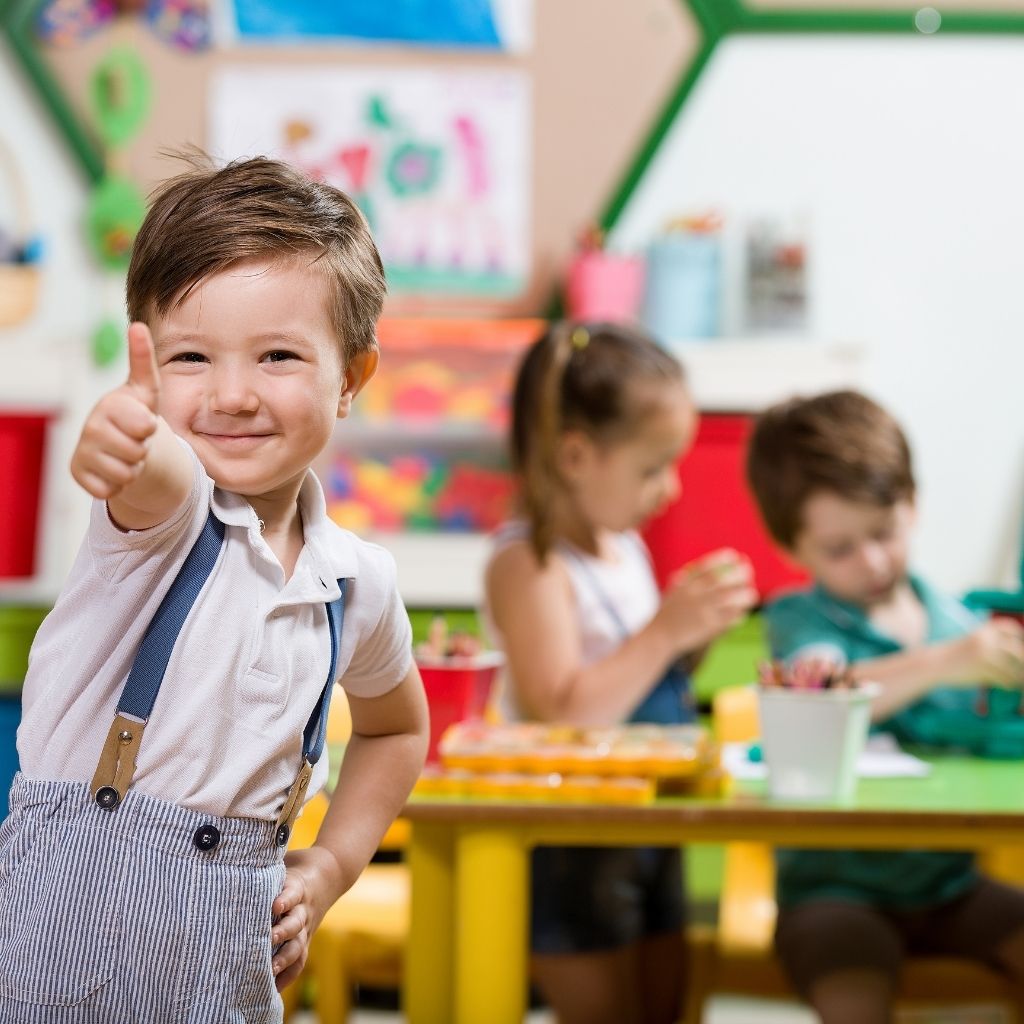 Preschool-aged child giving a thumbs-up while participating in a classroom activity