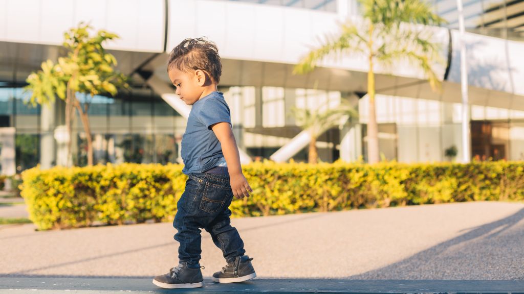 Young child walking alone outdoors near a building