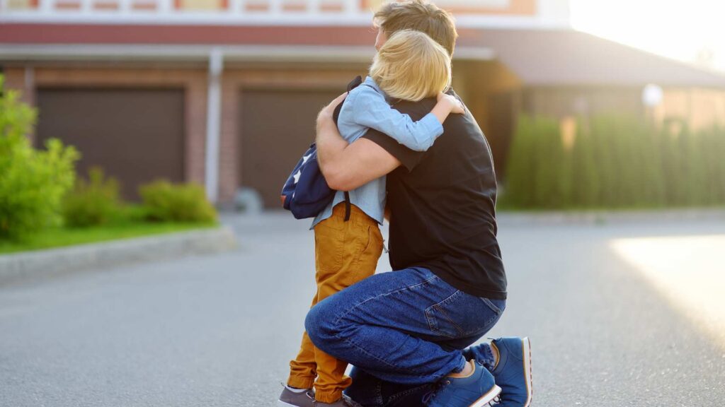 Parent kneeling on the ground hugging a young child during an emotional moment