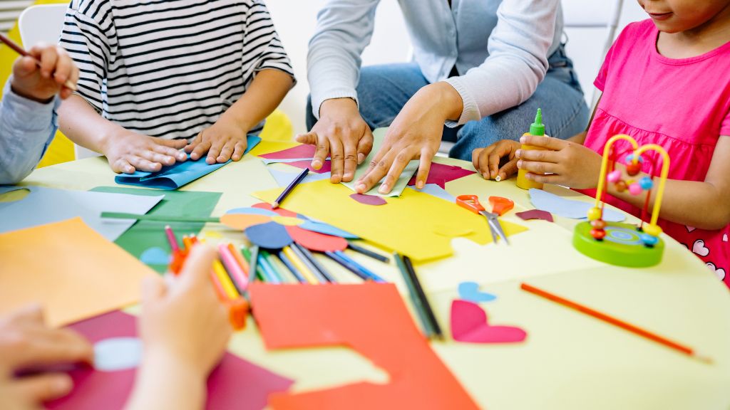 Children and teacher using colorful paper and classroom materials at a table