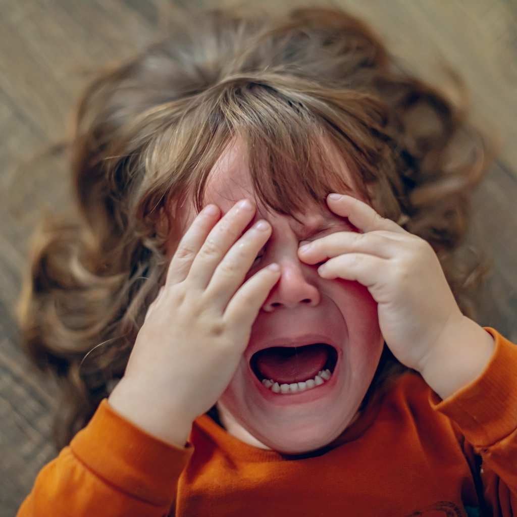A toddler crying with hands over their face, showing signs of sensory sensitivity in toddlers