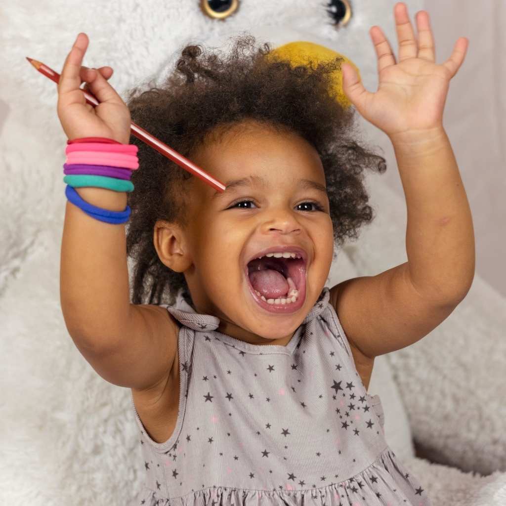 A toddler smiling with raised hands, showing playful behavior that may appear in both speech delay and autism