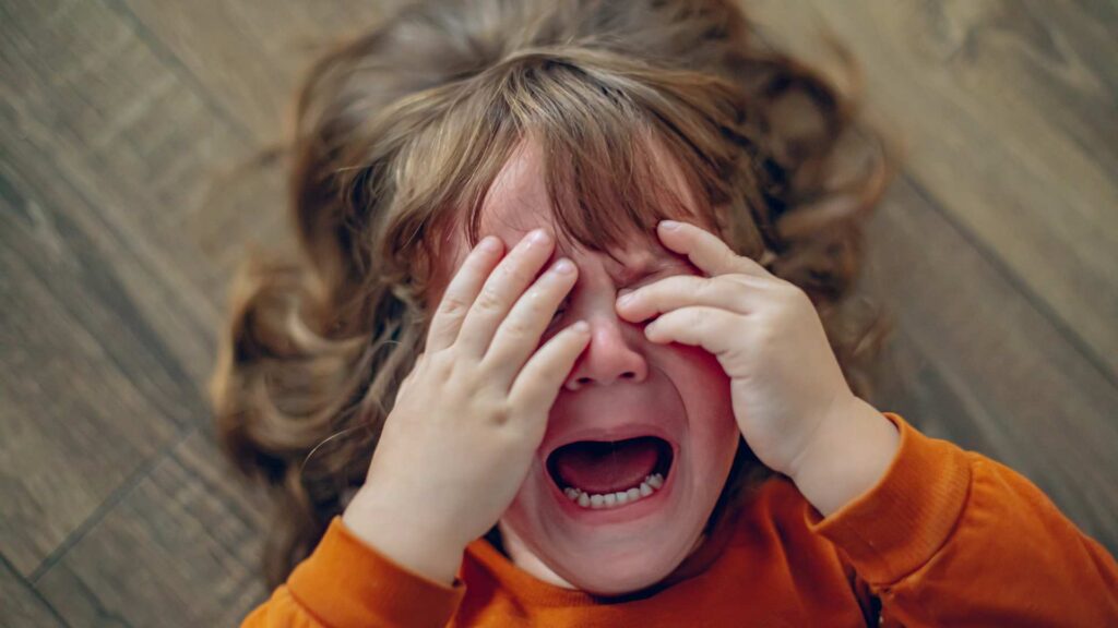 Child crying intensely on the floor, showing signs of emotional overload.