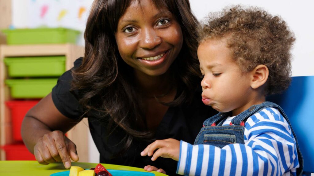 Adult and toddler at a table, with the toddler reacting strongly to food textures