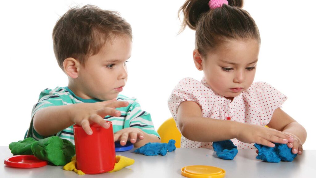 Two young children sitting side by side and playing with colorful clay
